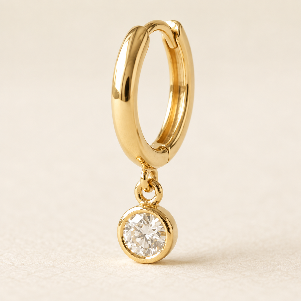 AI-generated visualization — close detail of the yellow-gold link and round bezel drop on a Bezel Drop Huggie.