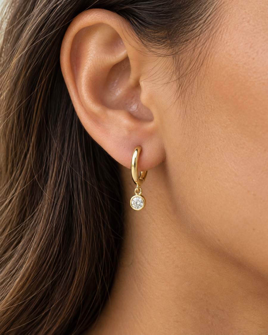 AI-generated visualization — a yellow-gold Bezel Drop Huggie worn on an adult ear.