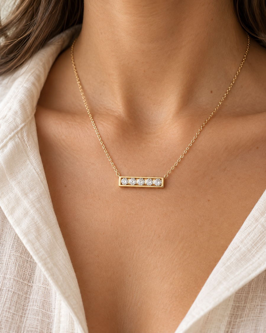 AI-generated visualization — yellow-gold Five-Stone Bar Necklace worn at the collarbone with an ivory shirt.