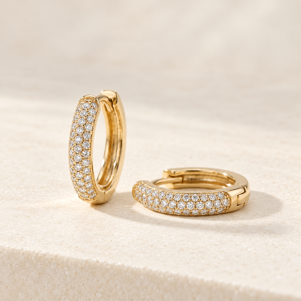 AI-generated visualization — yellow-gold Pavé Huggie Hoops on an ivory studio display.