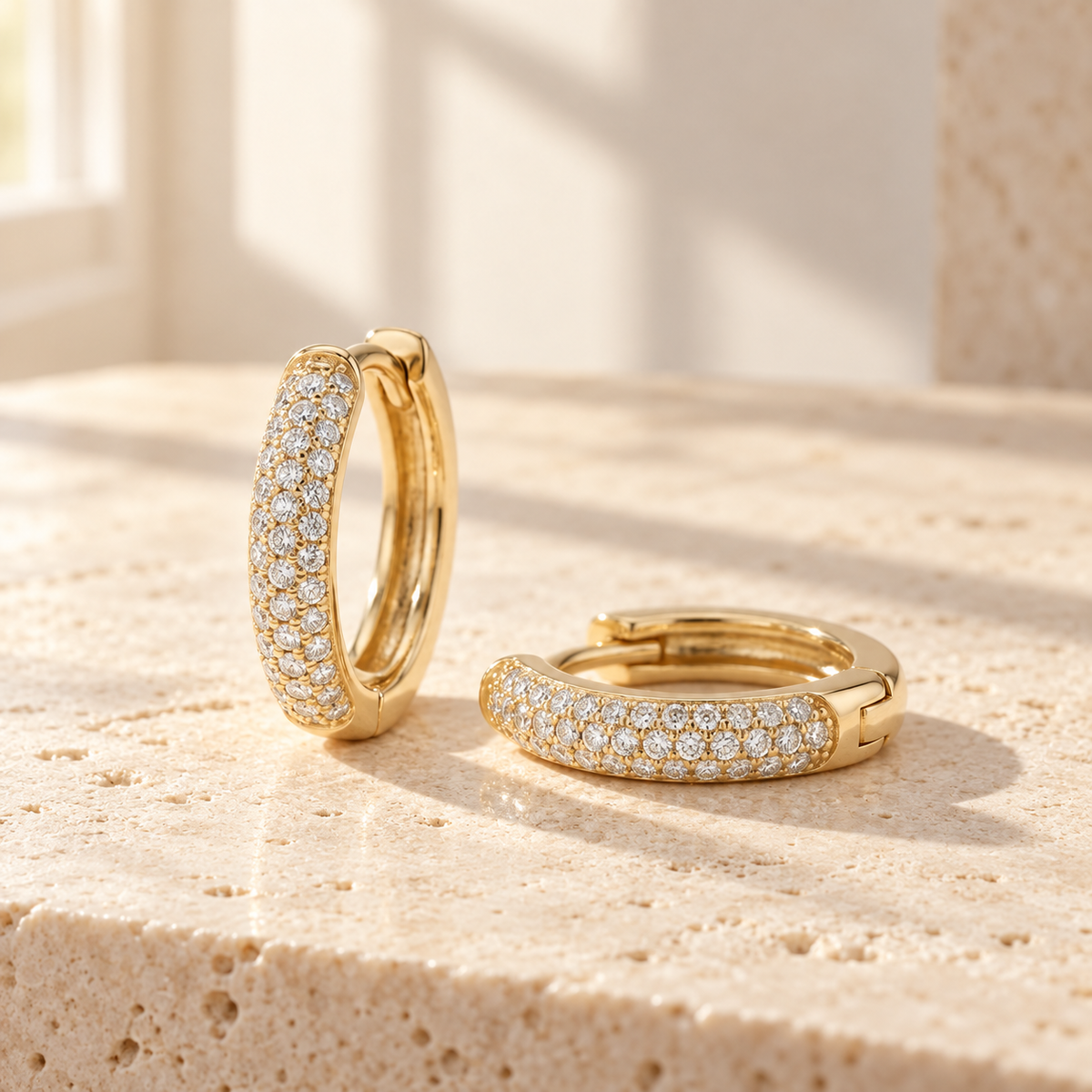 AI-generated visualization — a pair of yellow-gold Pavé Huggie Hoops on a warm tabletop in natural window light.